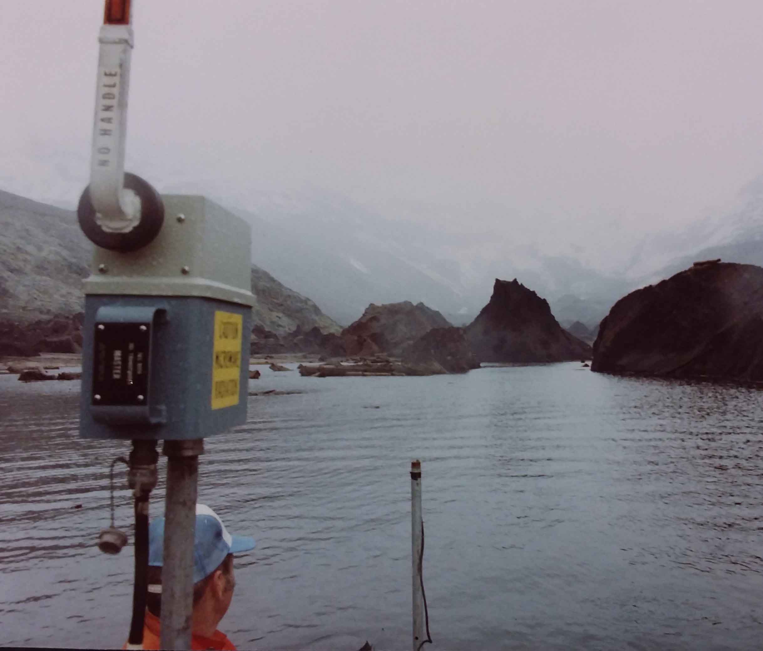 Mid-May 1981  Leonard Nelson in aluminum boat in Bear Cove, West Arm of Spirit Lake with debris avalanche hummocks. Microwave trisponder range finder in boat for use in bathymetric mapping.  USGS K. Tanner